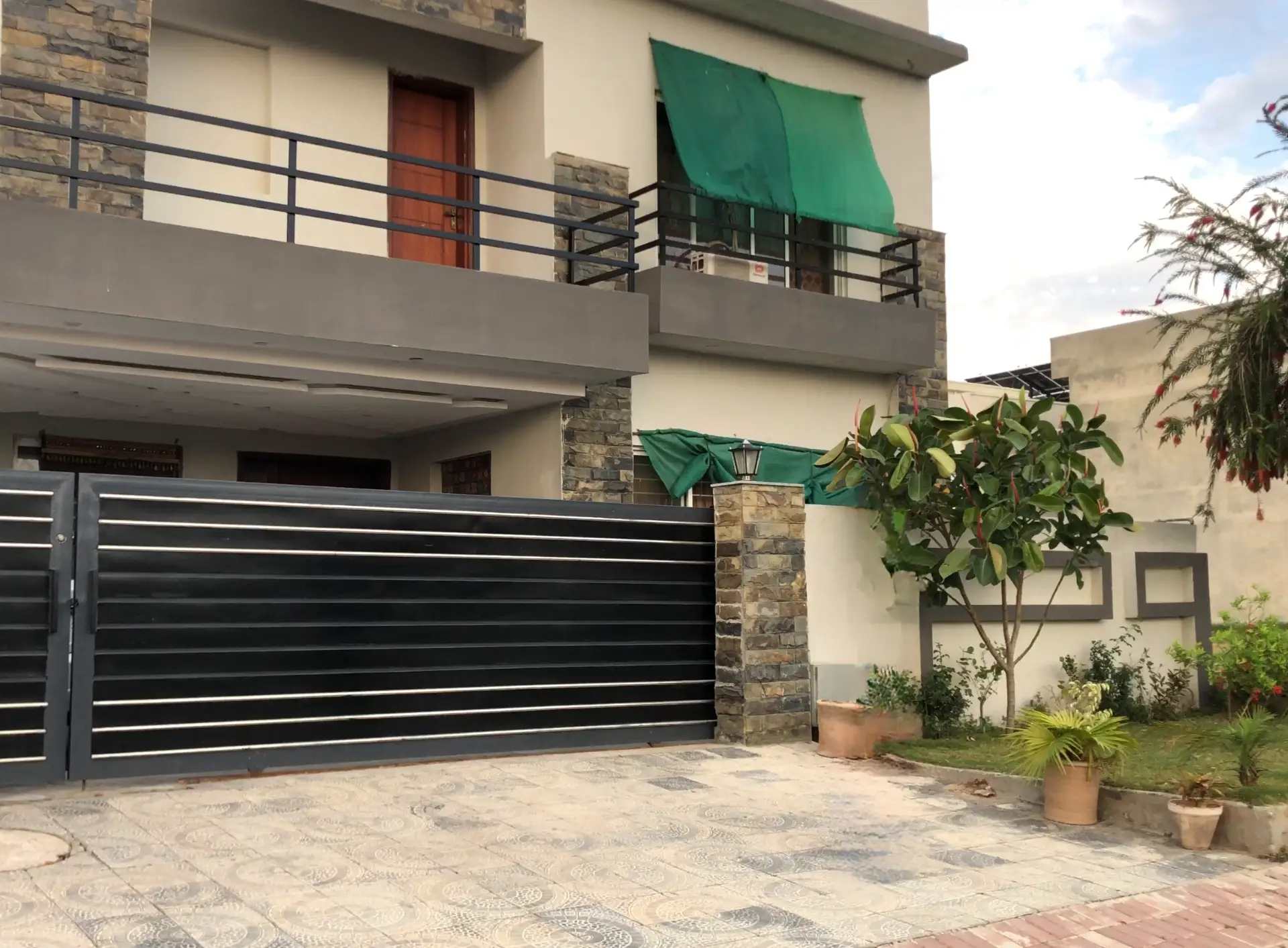 Front exterior of 10 Marla house in Sector F Bahria Town with stone-texture façade and black metal gate on boulevard road
